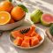 Ilustrasi jeruk, pepaya, jambu biji, dan brokoli sebagai sumber makanan dalam pembahasan fungsi vitamin C.